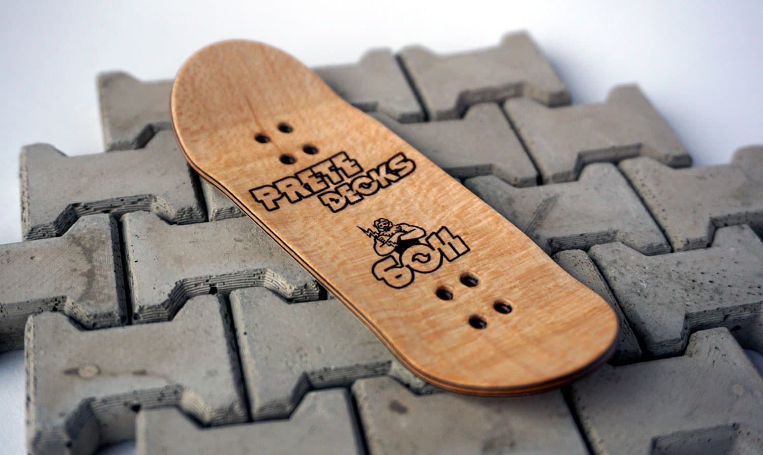 A raw maple Prete Decks 6011 fingerboard deck laser-etched 'PRETE DECKS 6011', resting on a bed of miniature concrete obstacles.