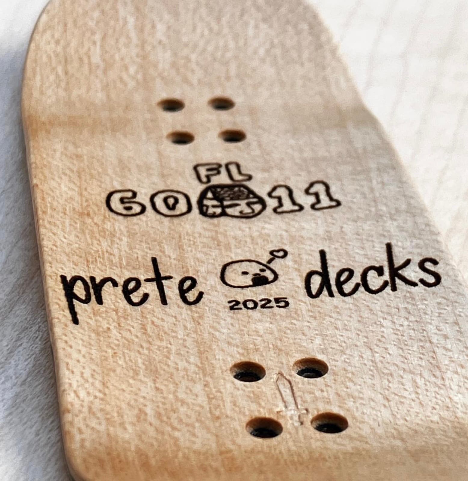 Close-up of a Prete deck underside laser-etched 'FL 6011', 'prete decks', a rice-ball mascot, and the year 2025.