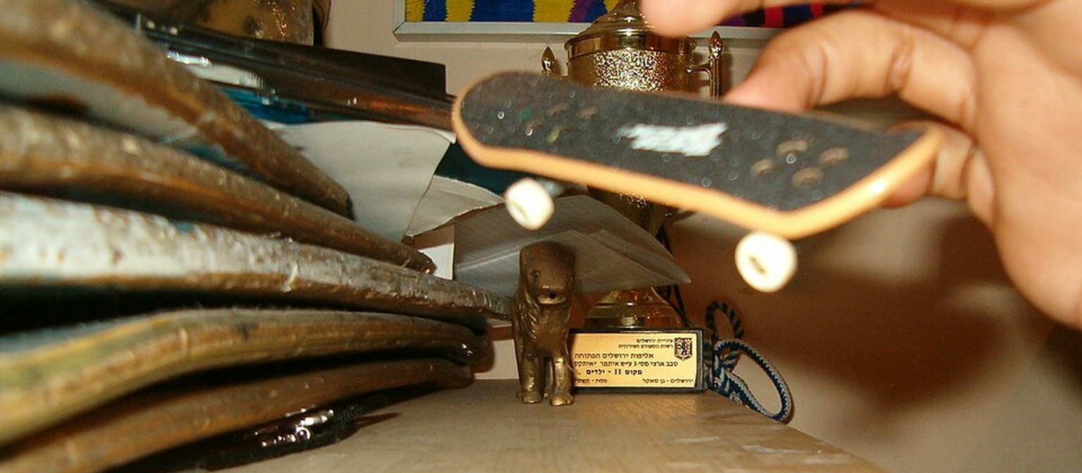 A hand riding a fingerboard across a homemade indoor obstacle.