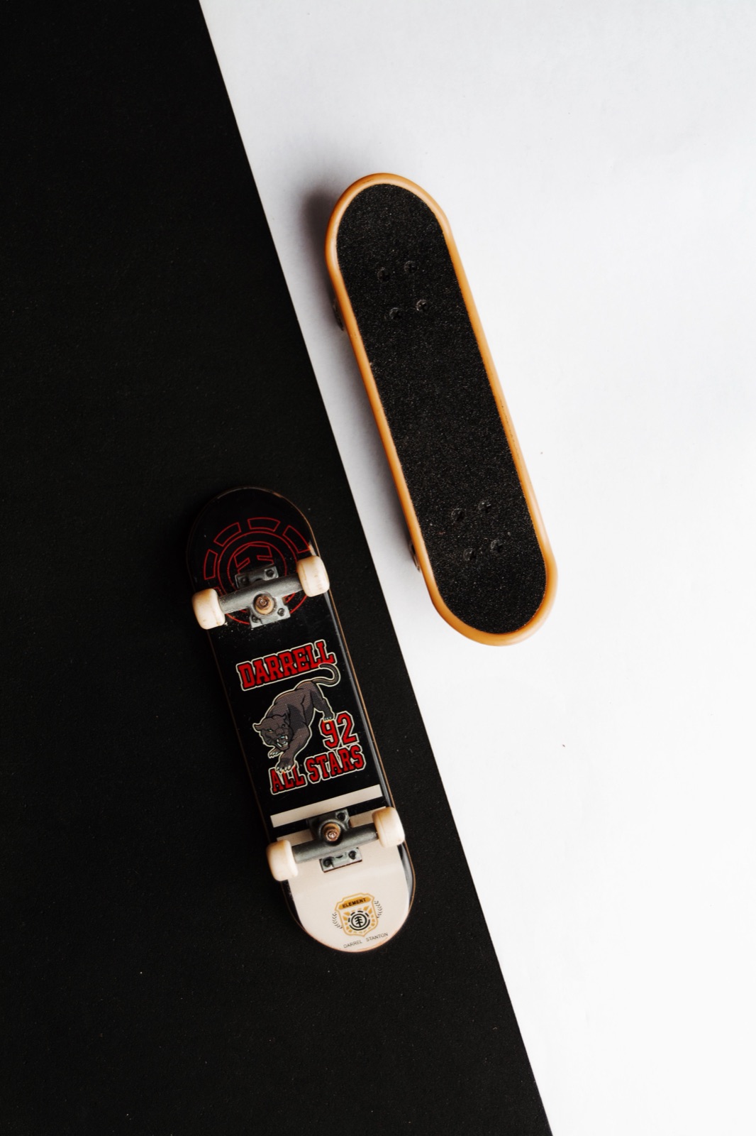 Two miniature fingerboard skateboards seen from above on a black-and-white surface.